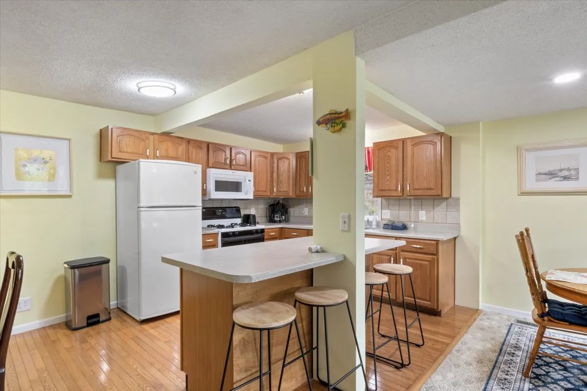 A cozy kitchen scene emphasizing the kitchen island, warm wood cabinetry, and modern appliances. The space is set up for both cooking and casual interaction, with subtle decorative touches creating a homey feel.