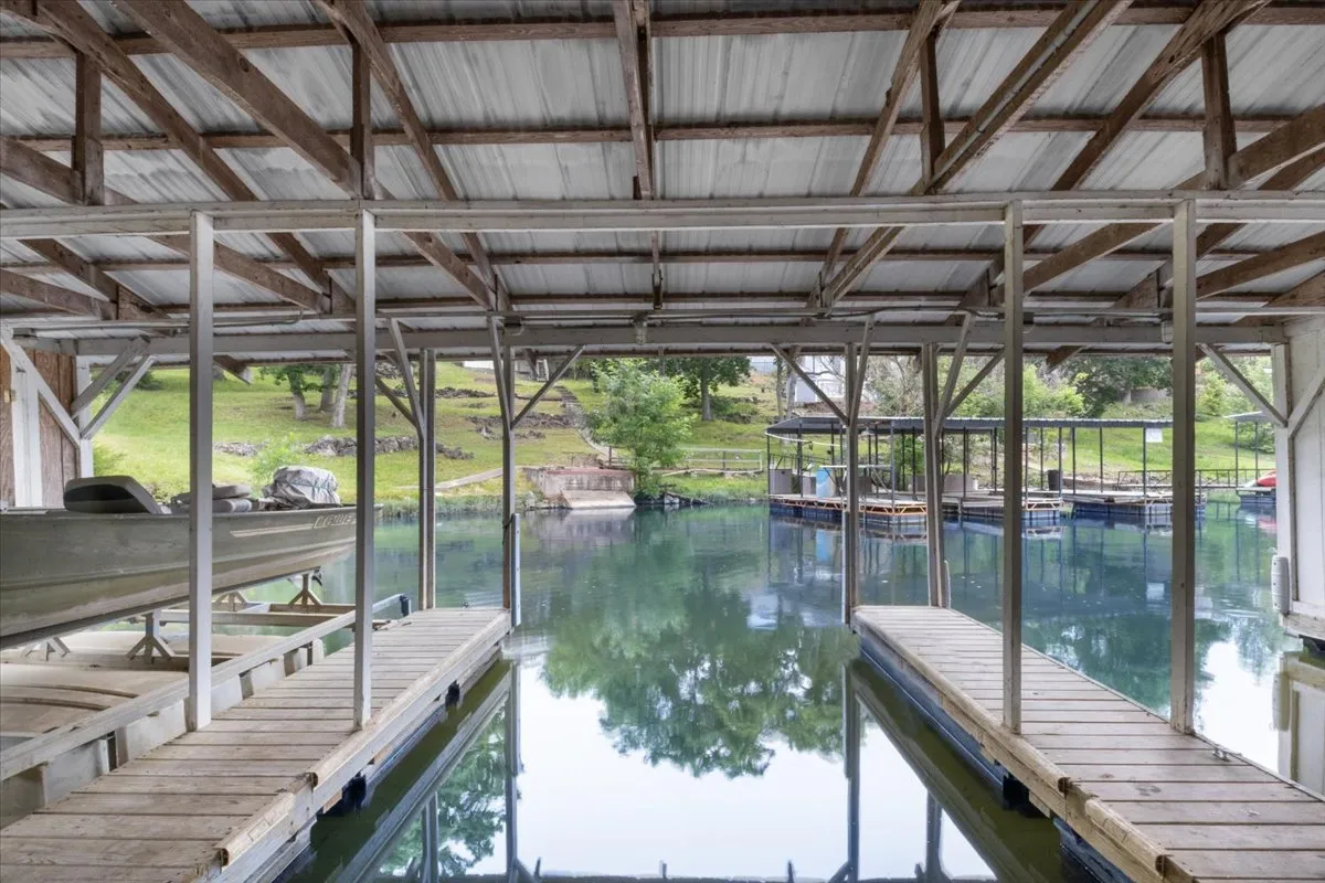 A serene lakeside dock with boats, water reflections, and lush green landscape. The scene evokes activities such as boating, fishing, and soaking up the beauty of the water, with community dock structures visible and the sense of peaceful waterfront living.