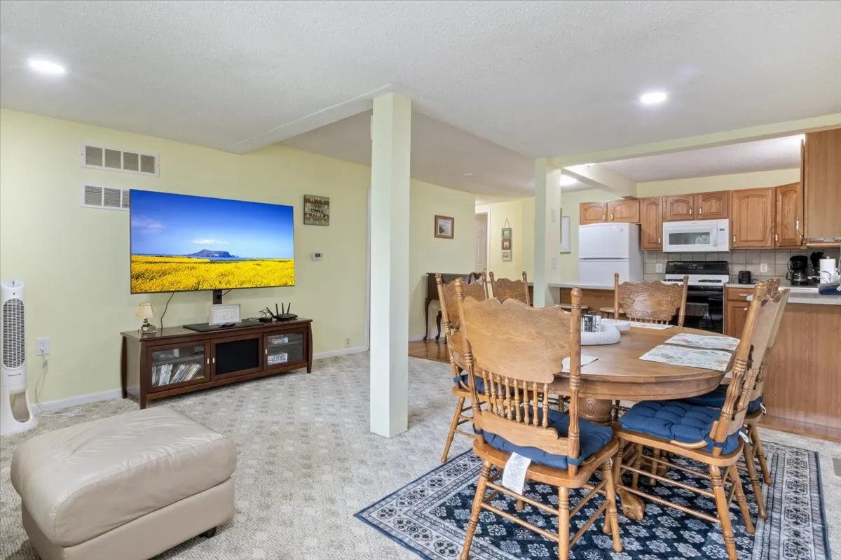 A welcoming area featuring a large television, wooden dining table with chairs, and a comfortable ottoman. The arrangement is ideal for family meals, movie nights, and casual get-togethers, reflecting an open, communal atmosphere that invites both relaxation and entertainment.