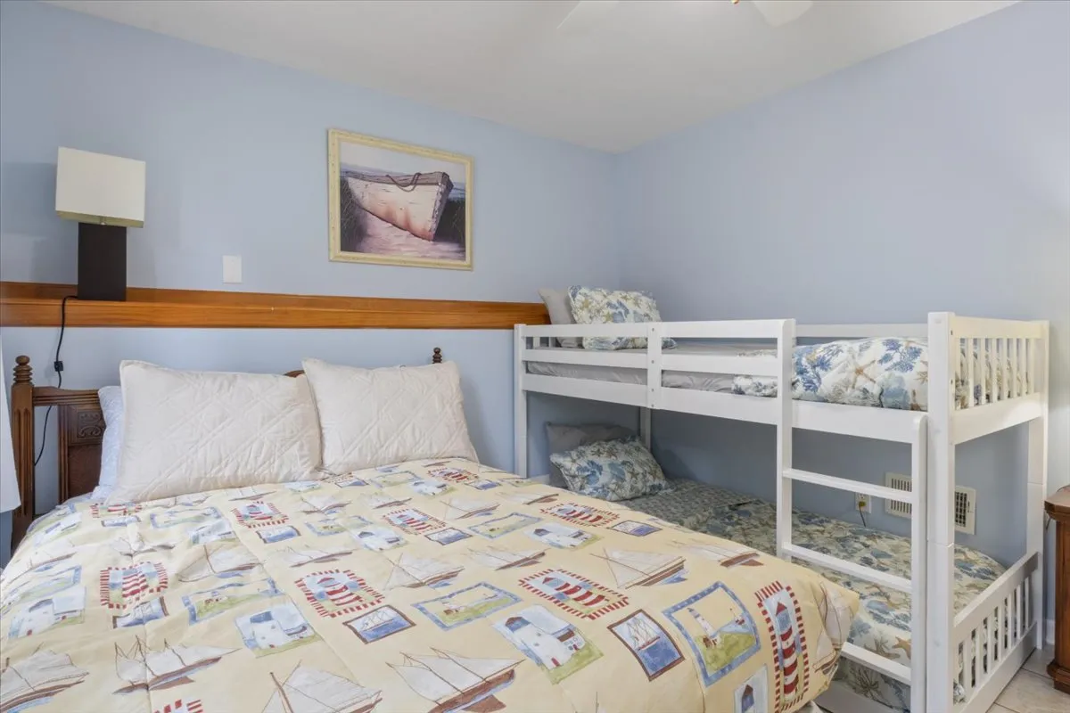 The image displays a large bed with crisp white bedding alongside a bunk bed, making it ideal for families or groups. Sunlight streams in, illuminating the room and creating an airy, family-friendly sanctuary.