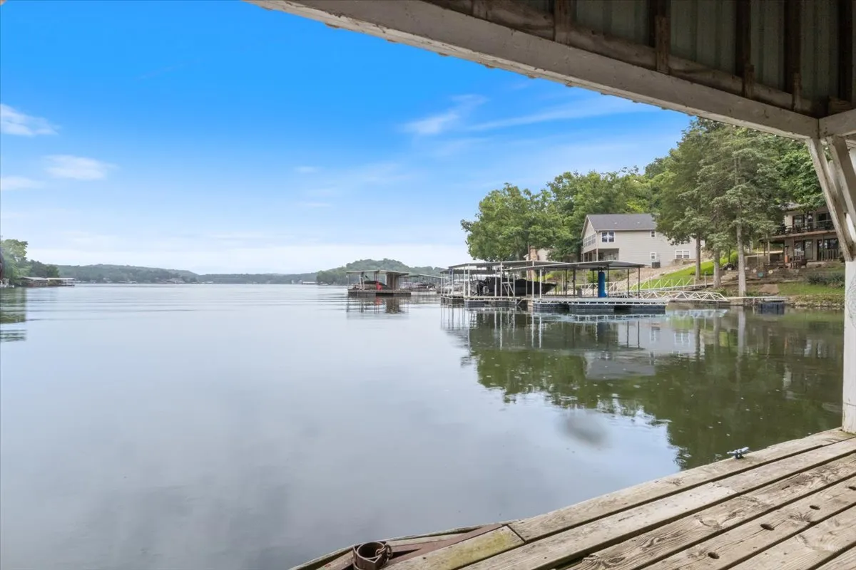 A broad view of calm lake waters with docks, boats, and vibrant green trees lining the shore. Houses are visible along the shoreline, and the entire scene radiates serenity—ideal for kayaking, paddleboarding, or enjoying the dawn chorus.