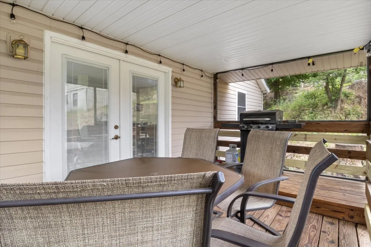 An exterior view featuring a dining table and chairs on the patio, a grill, and doors leading into the house. The setup is ideal for outdoor dining, socializing, or relaxing after a day of exploring the local community.