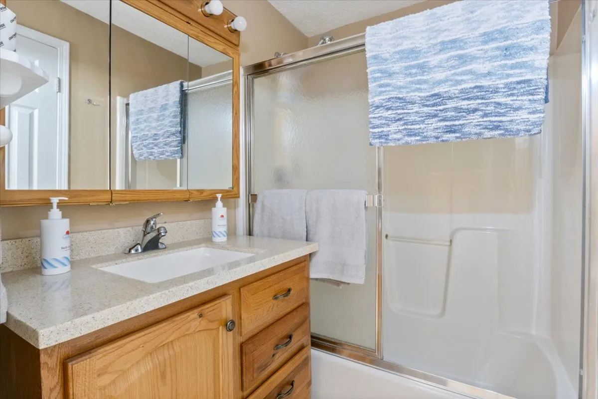 A well-appointed bathroom with a vanity sink, mirrors, shower area, and plush towels, all accented by a decorative rug. The space feels clean, inviting, and practical for shared use.