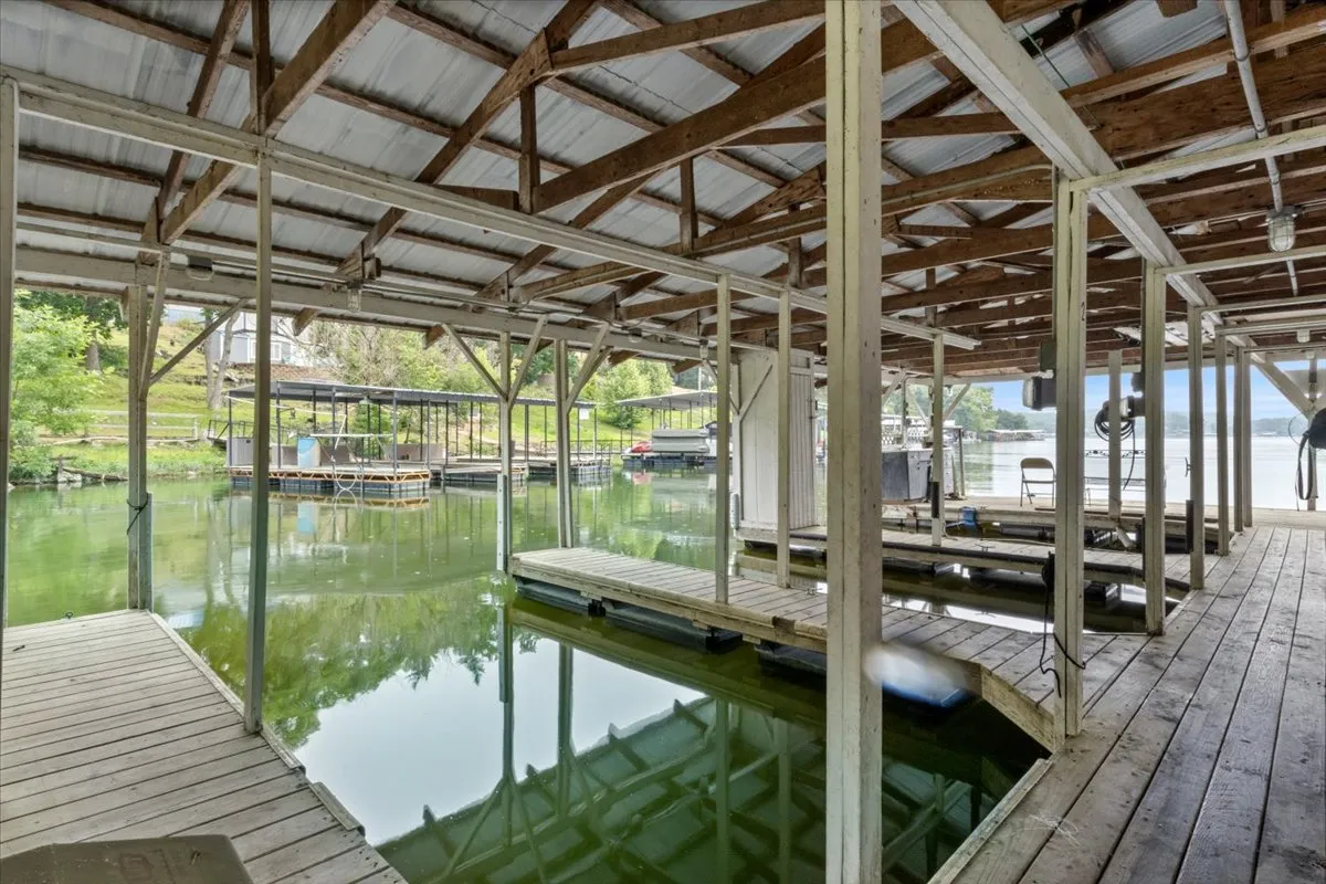 A serene view of the waterfront featuring wooden pillars extending into the lake, boat slips, and surrounding greenery. Reflections ripple across the water, hinting at quiet afternoons spent fishing or launching a boat. The relaxed, recreational vibe is evident, with the dock area clearly intended for family use.
