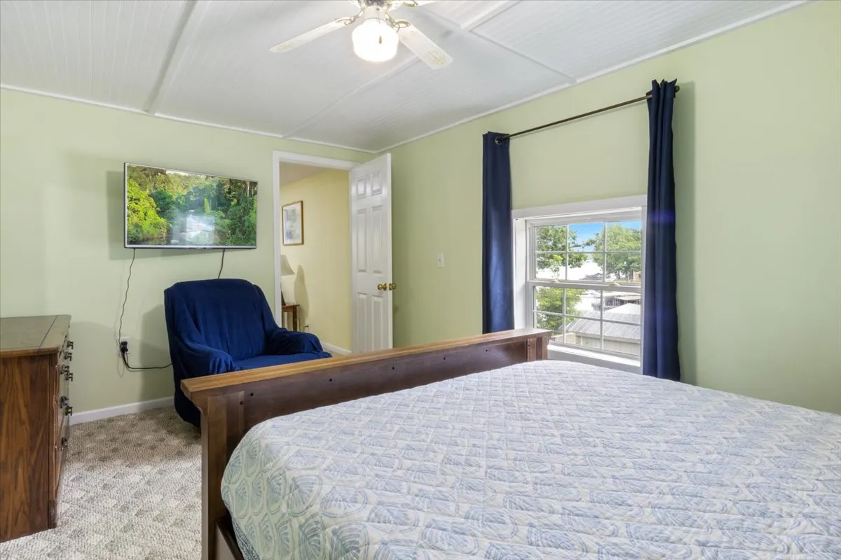 A tranquil bedroom with a comfortable bed, an armchair perfect for relaxing or reading, a television for entertainment, and a large window that lets in abundant natural light and offers a scenic view.