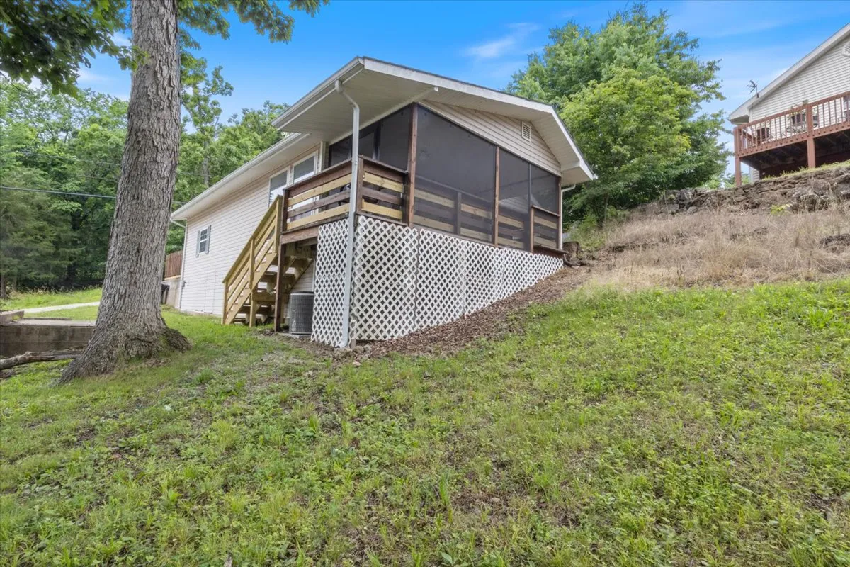 This image features a screened porch with wooden steps leading to lush green grass and trees, capturing the essence of a peaceful outdoor retreat. The porch is inviting and surrounded by nature, making it ideal for enjoying morning coffee or relaxed gatherings in a semi-outdoor setting.
