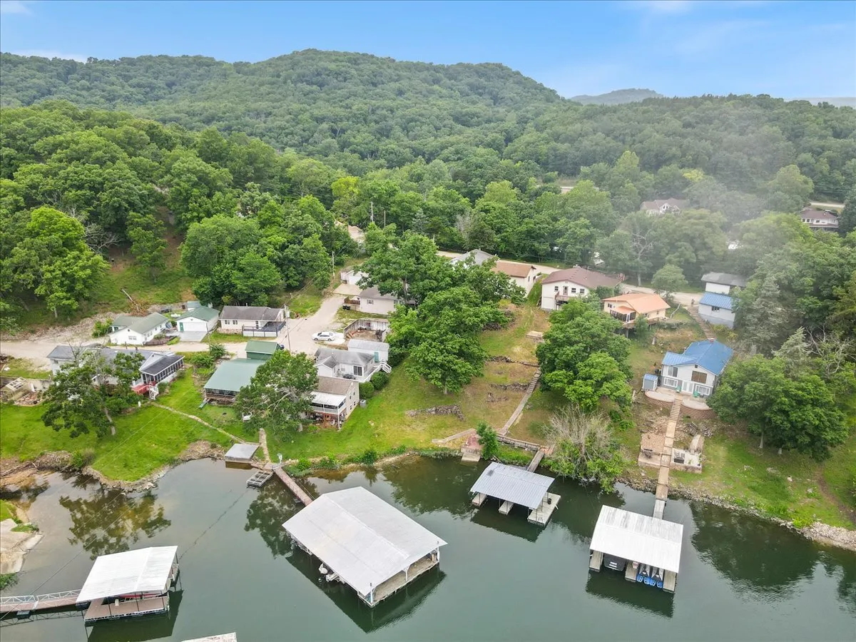 A tranquil view of the lake, with green hills in the background and a cluster of houses along the shoreline near boat docks. The scene evokes a sense of community and recreation, with ample opportunities for boating, fishing, and participating in lakeside events.
